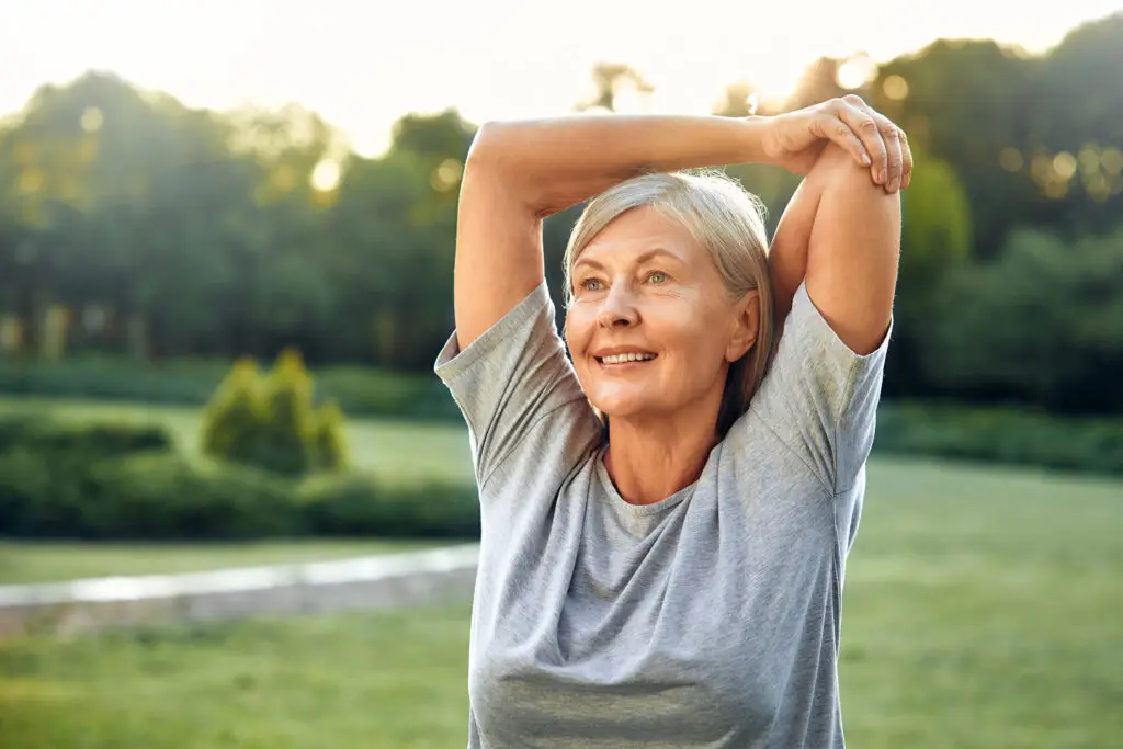 A Joyful Senior Woman Engaging in Stretching Exercises Amidst Nature During the Morning